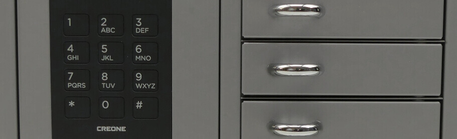 Detailaufnahme eines CREONE Schließfachsystems mit Zahlentastenfeld und drei Metallschubladen mit silbernen Griffen